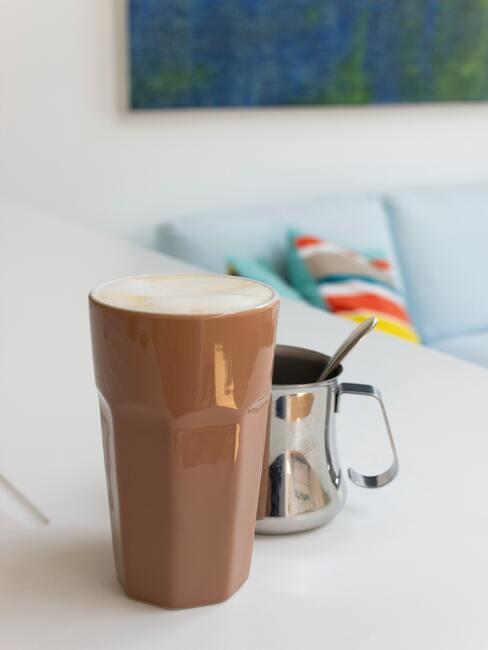 Wysoka, brązowa szklanka z chai latte, na białym blacie