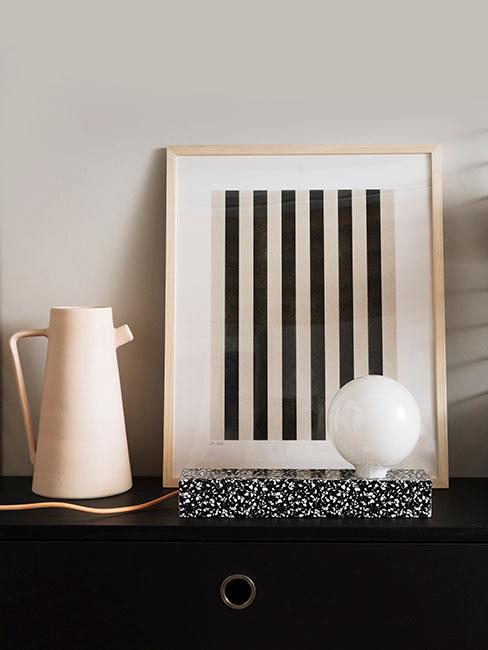 Beżowy dzbanek z kamionki i oprawiony dreuk przedstawiający czarne równoległe linie w minimalistycznym stylu