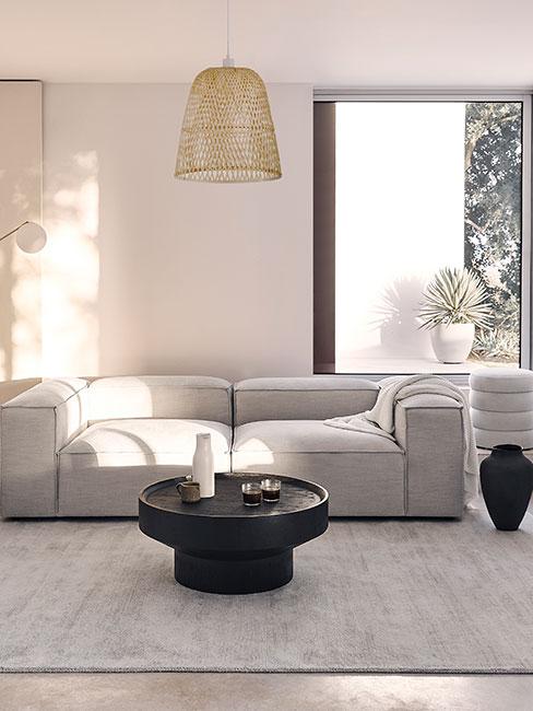 Szara sofa modułowa z niskim okgrągłym czarnym stołem kawowoym z drewna w jasnym salonie