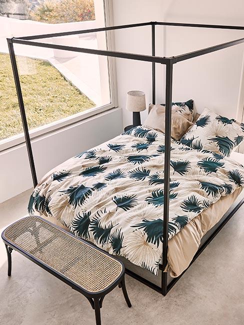 Carne łóżko z baldachimem w jasnej sypialni z czarną ławką z plecionką wiedeńską i pościelą w liście palm