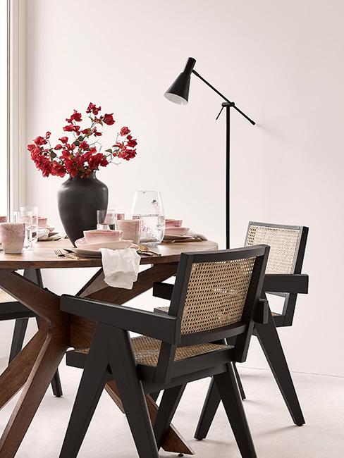 okrągły stół do jadalni z brązowego drewna otoczony czarnymi drewnianymi krzesłami z plecionką wiedeńską z czarnym wazonem z kamionki na stole