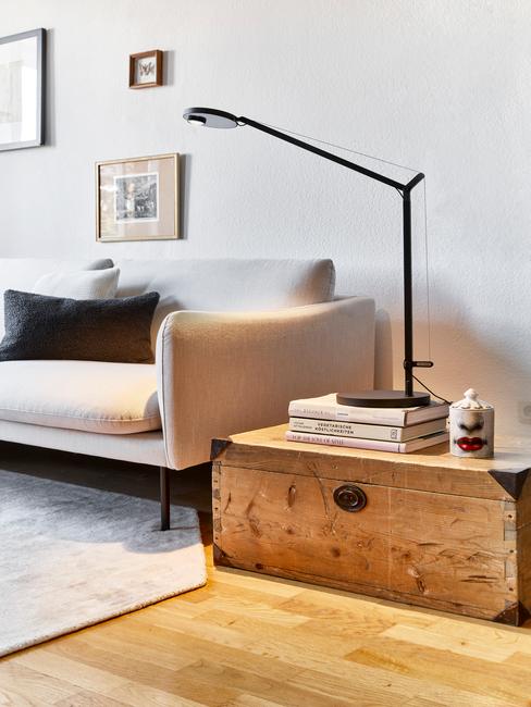 Zbliżenie na szarą sofę z czarną poduszka, jasnym dywanem oraz drewnianą szafką