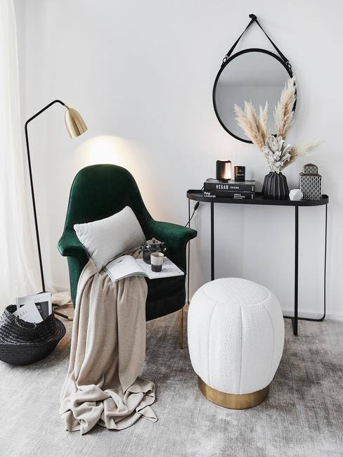 Zbliżenie na kącik ze szmaragdowym krzesłem, kocem, złotą lampą, czarną konsolą i lustrem