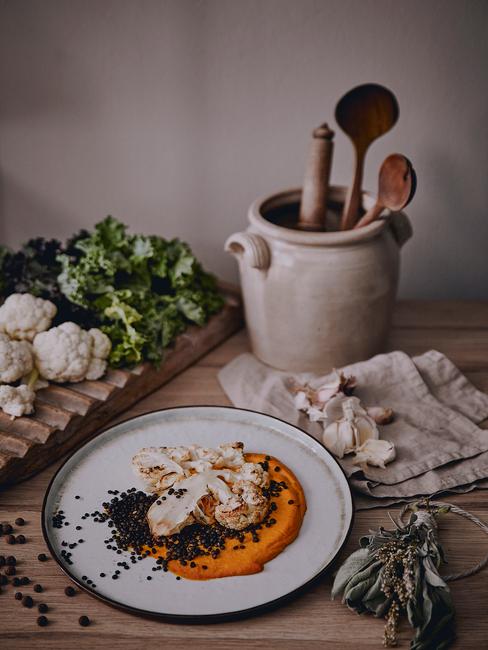 Białytalerz z hummusem z dyni oraz pieczony kalafior obok dzbanka z drewnianymi łyżkami