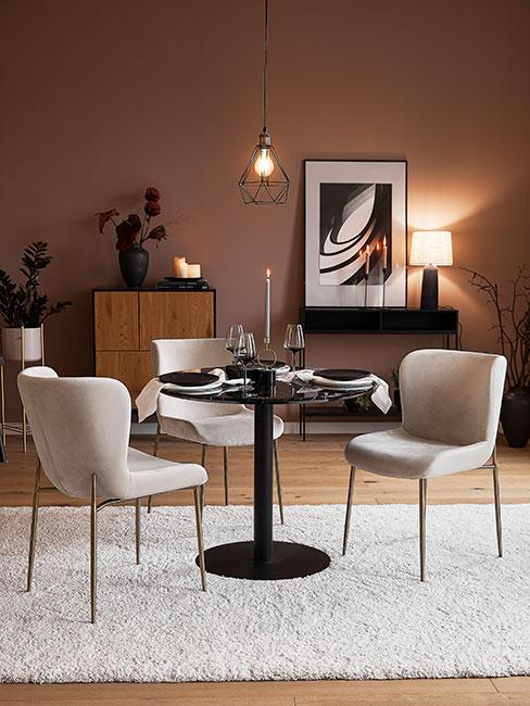 Jadalnia z małym czarnym okrągłym stołem z marmuru, krzesłami z beżowego aksamitu na tle brązowej ściany i drewnianych mebli