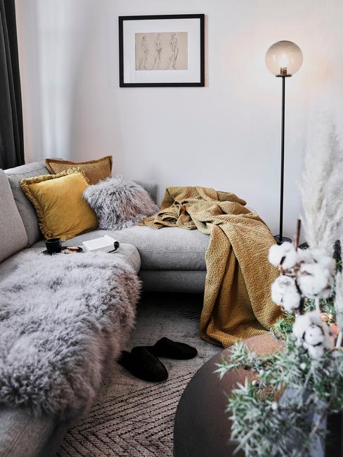 szara sofa narożna z szarym futerkiem i żółtymi tekstyliami