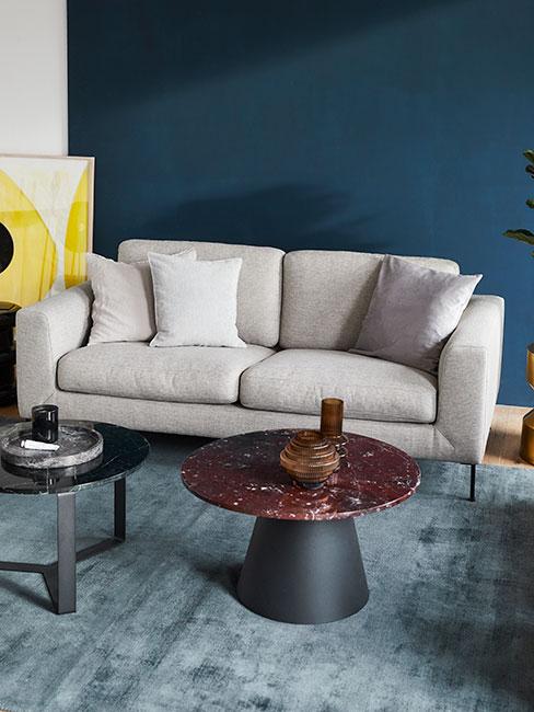 Szara sofa na tle niebieskiej ściany ze stolikiem bordo