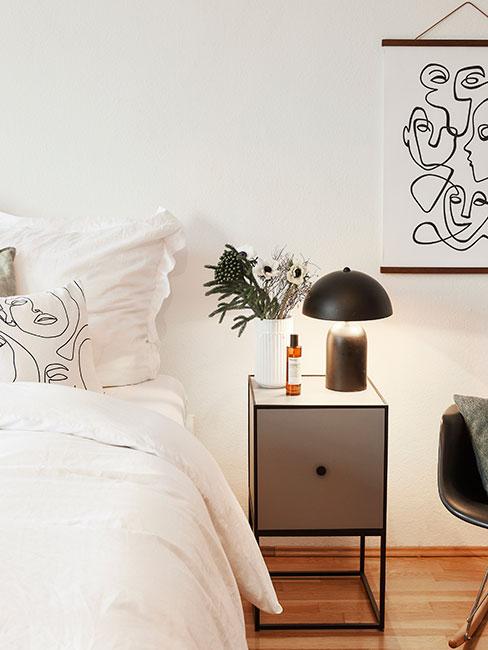 Zbliżenie na minimalistyczną szarą szafkę nocną i czarną lampę obok łóżka z białą pościelą