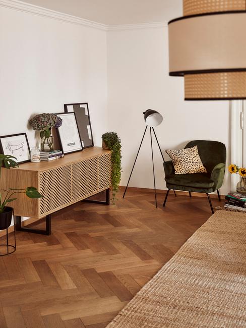 Fragment sypialni, gdzie znajduje się drewniana komoda z galerią zdjęć, fotel z lampą oraz boho żyrandol