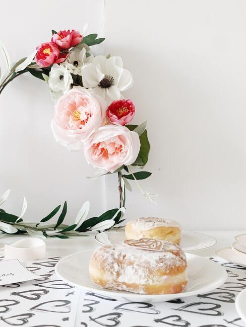 Białe pomieszczenie z wiankiem na ścianie oraz białym talerzem z ciastkami