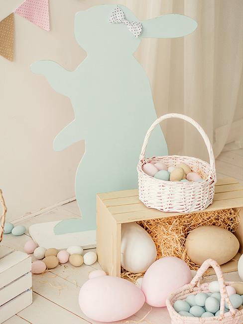 pastelowy papierowy królik za skrynią z iwlkimi pastelowymi jajkami obok niałego koszyka