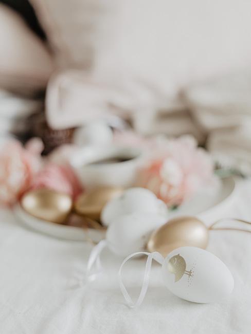 złote i białe jajka wielkanocne na tle różowych kwiatów