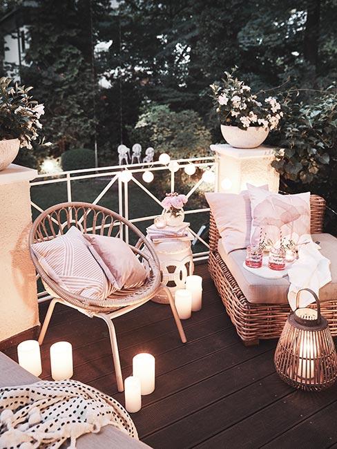 Przytulny balkon óświetlony świeczkami i lampkami z rattanowymi meblami i różowymi poduszkami