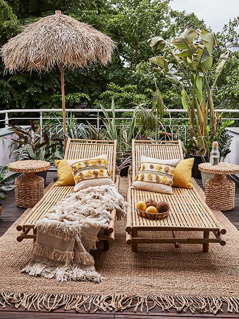 Balkon z dwoma leżakami z bambusa, parasol oraz jutowy dywan zewnętrzny z roślinami
