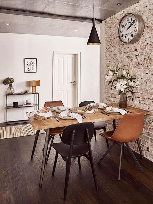 Jadalnia industrialna z jasnym drewnianym stołem z ciemną drewnianą podłogą i ceglaną ścianą