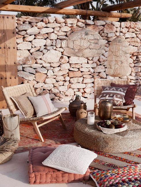 Taras w stylu boho ze ścianą z kamienia i beżowymi meblami z bambusa i juty