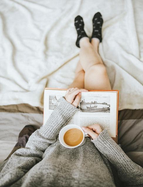 Kobieta czytająca książkę w łóżku z kubkiem kawy