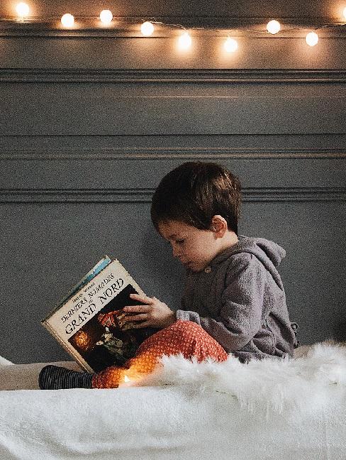 Chłopczyk siedzący na łóżku i czytający najlepsze bajki