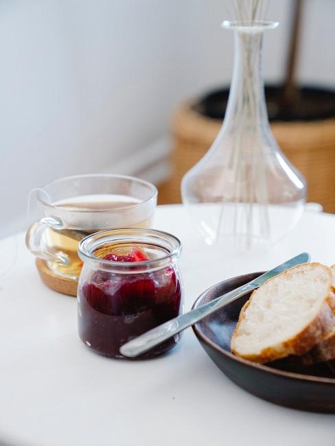 Dżem truskawkowy w małym słoiczku obok herbaty i talerza z pieczywem