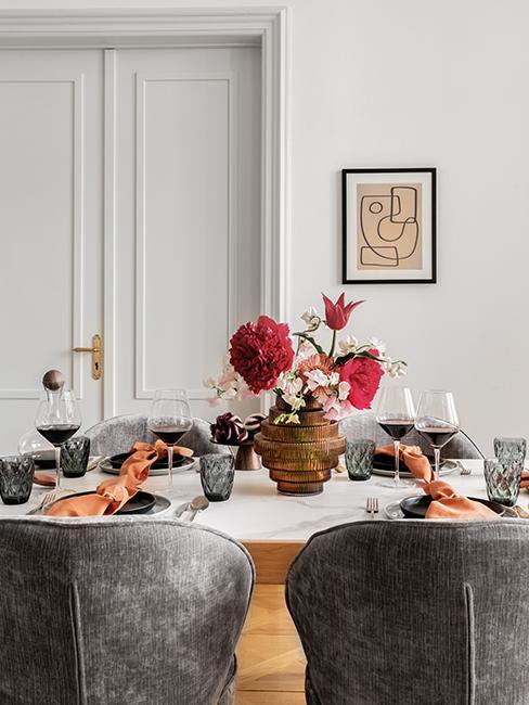 zbliżenie na bursztynowy wazon z kwiatami na białmy stole przy którym stoją szare krzesła