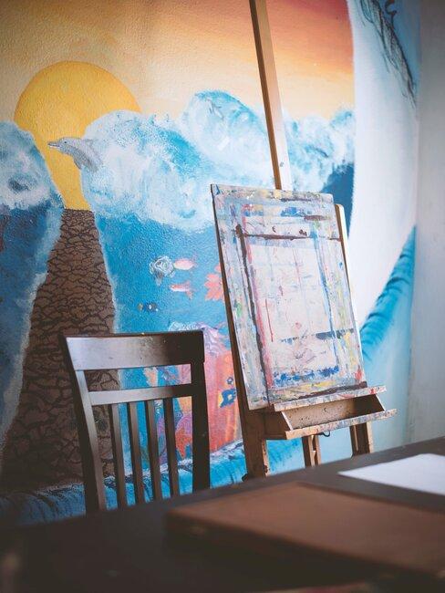 Ściana udekorowana malunkiem, obok niej sztalugi do malowania