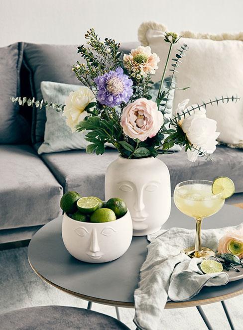 żółty drink z cytryną na stoliku kawowym obok białego wazonu z kwiatami