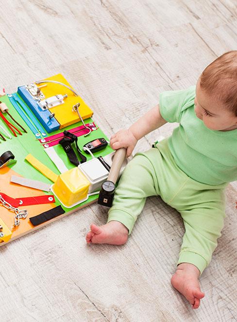 niemowlak siądzący na podłodze obok tablicy manipulacyjnej