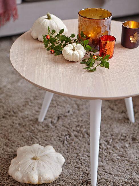 jasny stół na którym stoją małe dynie zielona gałązka i świeczki