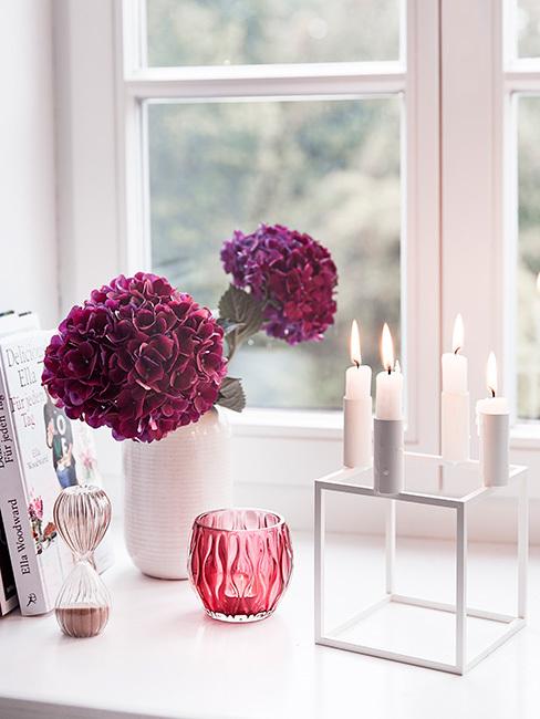 burgundowe kwiaty w białym wazonie na paprapecie obok minimalistycznego białego świecznika