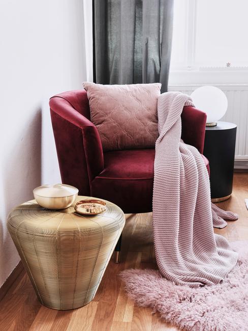 burgundowy fotel obok złotego stolika z różową narzutą
