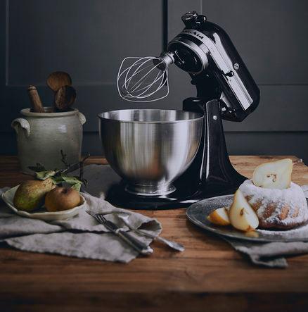 Czarny robot kuchenny w biało czarnej kuchni, na drewnianym blacie, na tle czarnej ściany