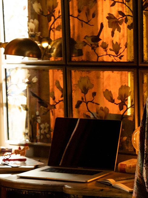 Steampunk: wnętrze z ozdobną zasłoną w kolorze pomarańczowym w kwiaty i ptaki, stół drewniany z laptopem na blacie