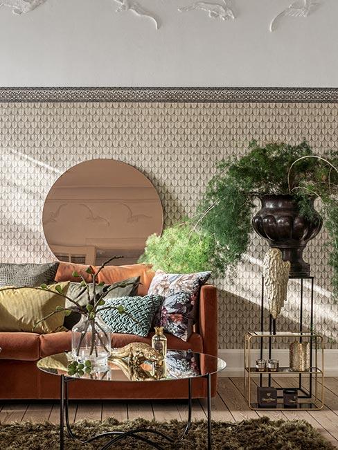 sofa w kolorze rdzy z poduszkami w koloracj jesieni obok wazonu z dużą rośliną