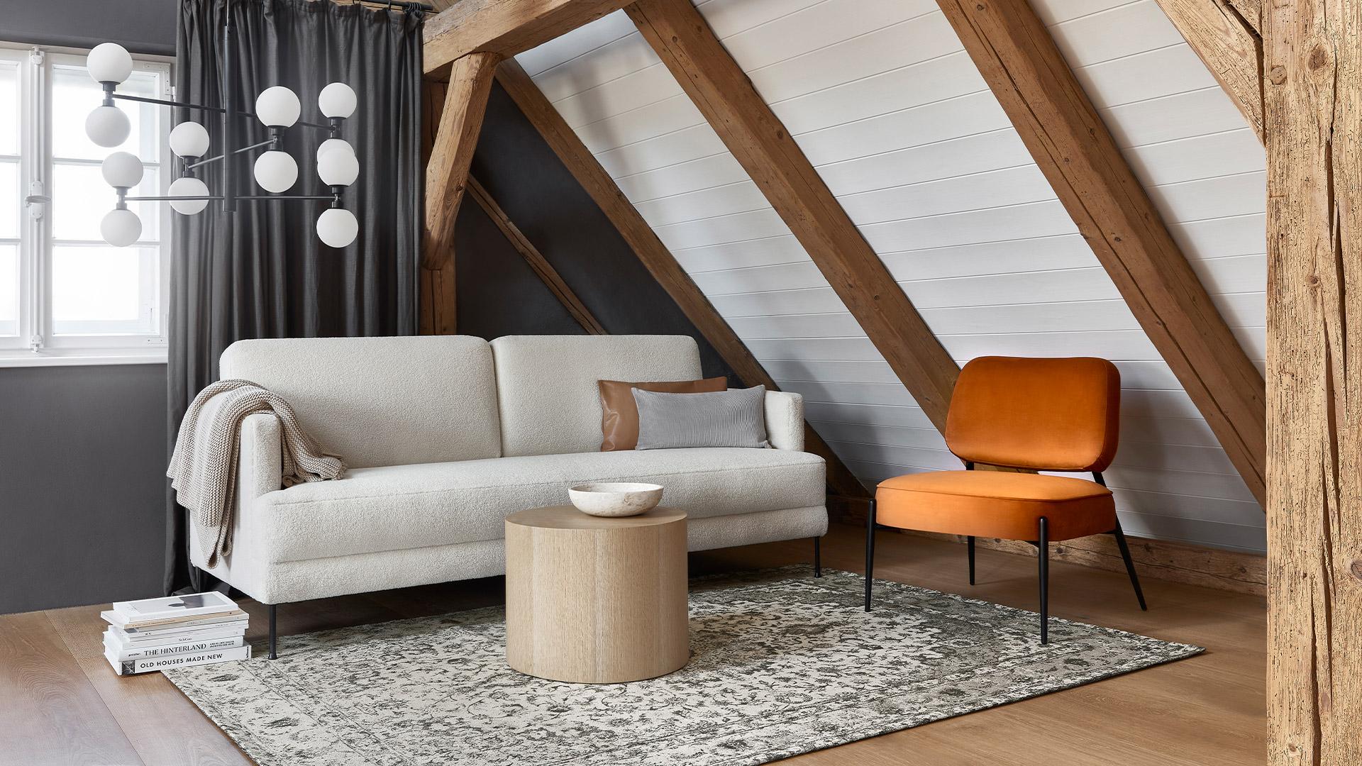 beżowa sofa na poddaszu w lofcie przy pomarańczowym krześle z aksamitu