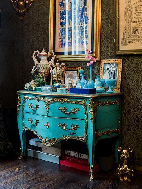 Komoda w stylu rokoko w morskim kolorze z mosiężnymi zdobieniami, na niej dekoracje w różnych kolorach