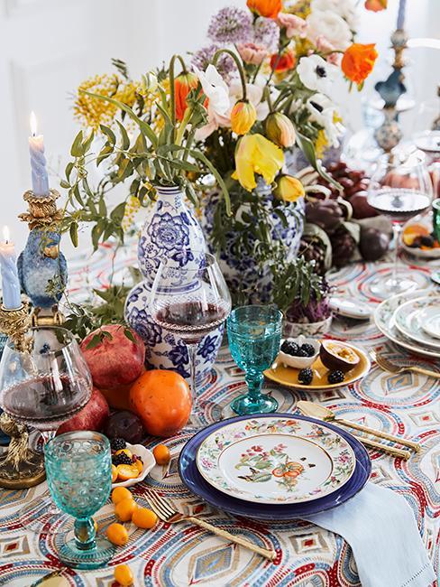 Stół zastawiony kolorową zastawą, ozdobnymi wazonami i obrusem w w kolorowe wzory