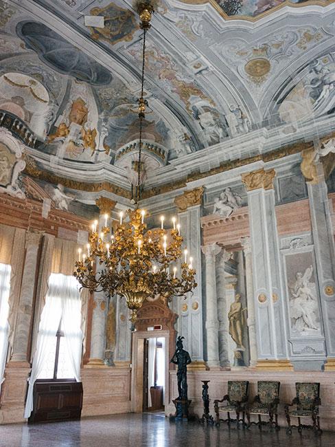 wnętrze w stylu rokoko, ściany bogato zdobione malunkami w kolorze białym, niebieskim i różowym, na suficie żyrandol