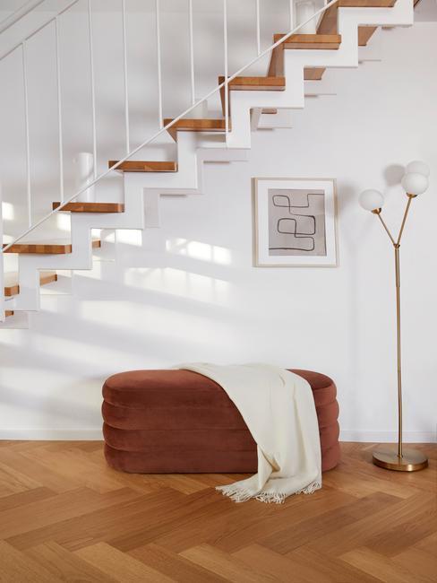 przestrzeń obok schodów urządzona minimalistycznie, mały brązowy puf , biały kocyk, złota podłogowa lampa