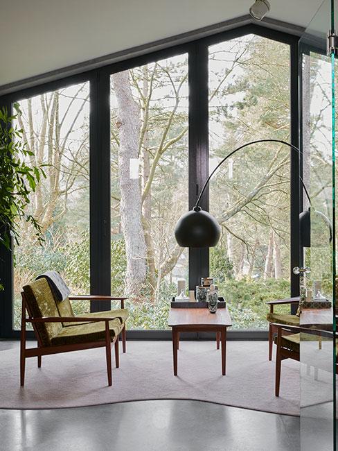 Salon w stylu loftowym, ciekawe fotele w zielonym odcieniu, mały stolik kawowy, cała ściana przeszklona