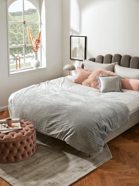 Sypialnia w stylu mid century modern, szare wezgłowie łóżka, szara narzuta, różowe dodatki, różowy puf