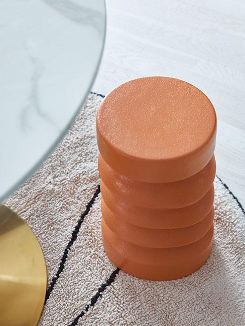 Pomarańczowy puf na dywanie obok stołu