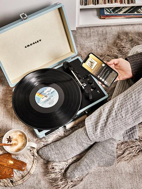 Gramofon z płyta winylową na łóżku obok człwoieka w skarpetkach i telefonem w dłoni