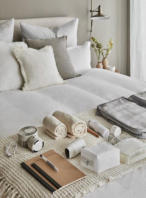 Otwarta walizka na łóżku przygotowana do pakowania z wentylatorkiem, klapkami, podróżną poduszką