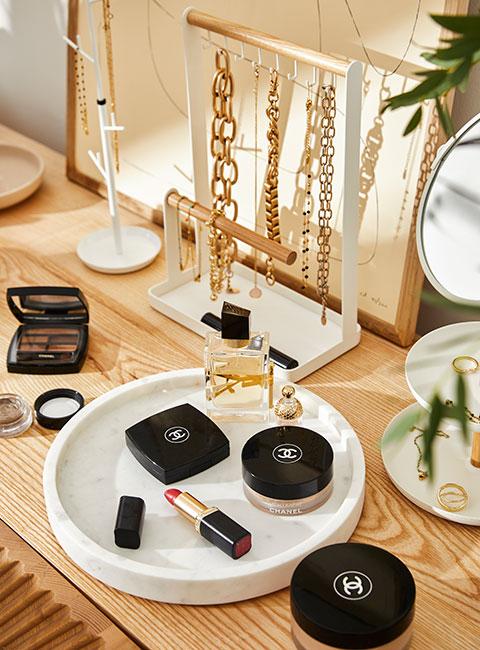 złota biżuteria na białych stojakach na biżuterie obok luksusowyh kosmetyków