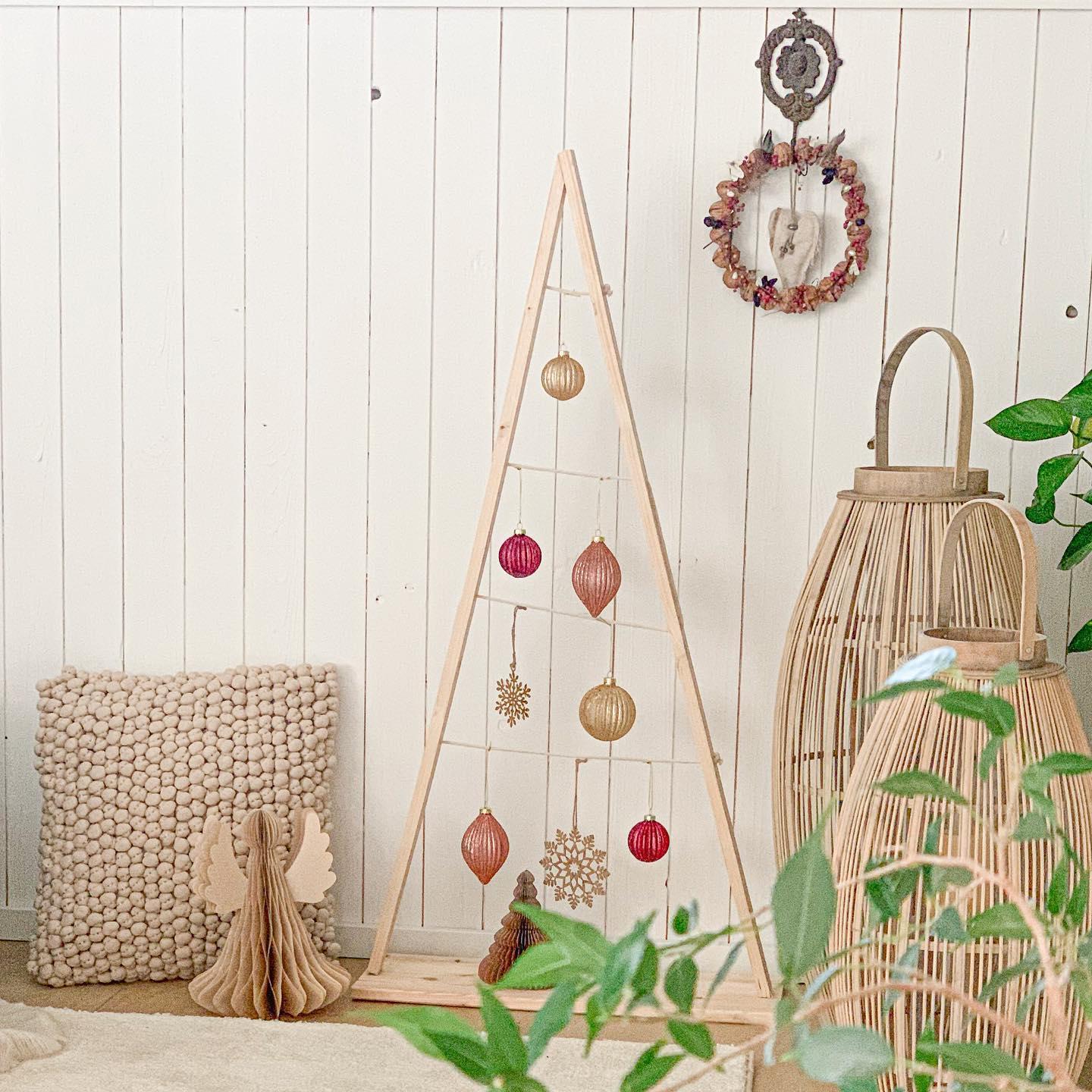 Stojąca choinka z desek ozdobiona różowymi bombkami w kąciku z latarenkami w stylu boho