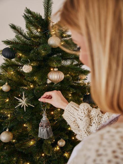 Kobieta w blond włosach i białym sweterku wieszająca ozdoby na choince