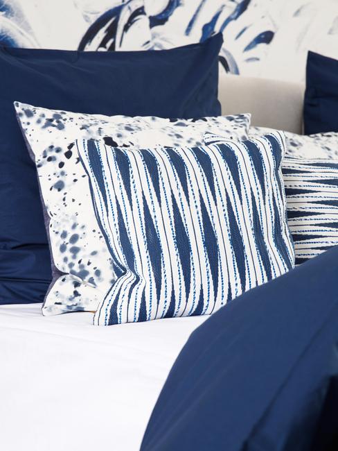 Wzorzyste poduszki, w kolorach białym i ciemnym niebieskim na łóżku z granatową pościelą