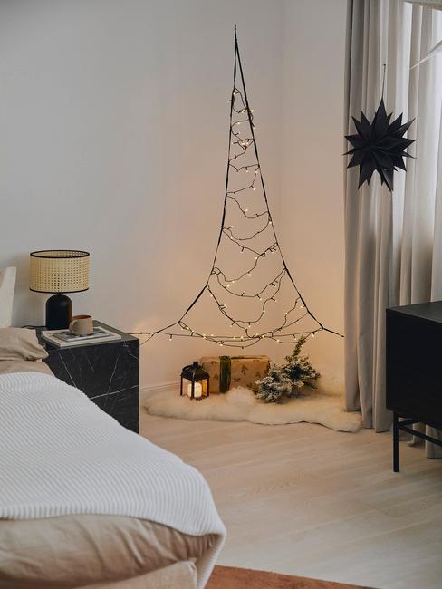 Choinka na ścianie w rogu pokoju zrobiona ze światełek, pod którą leżą prezenty