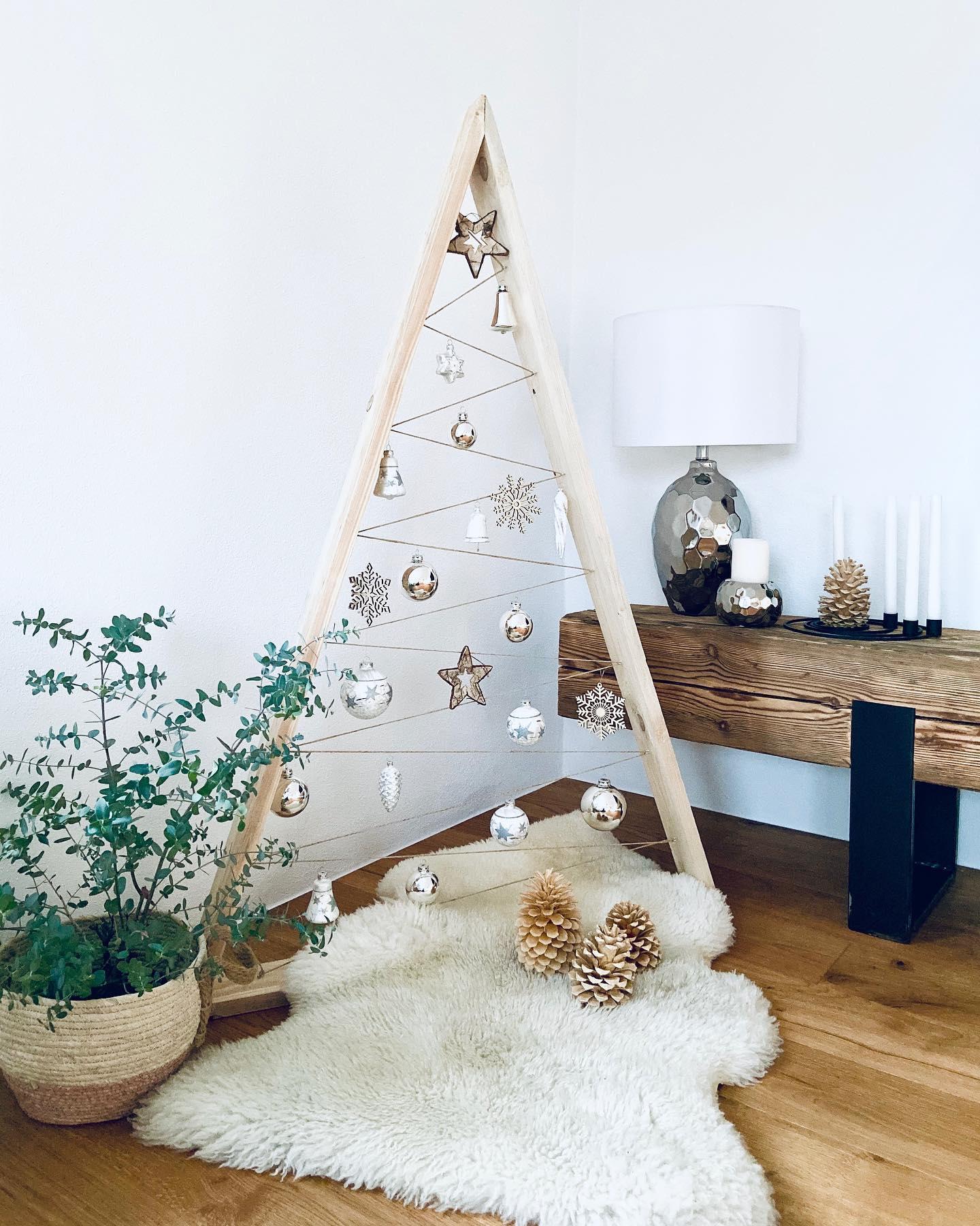 Stojąca choinka z desek ozdobiona beżowymi bombkami w kąciku w stylu boho