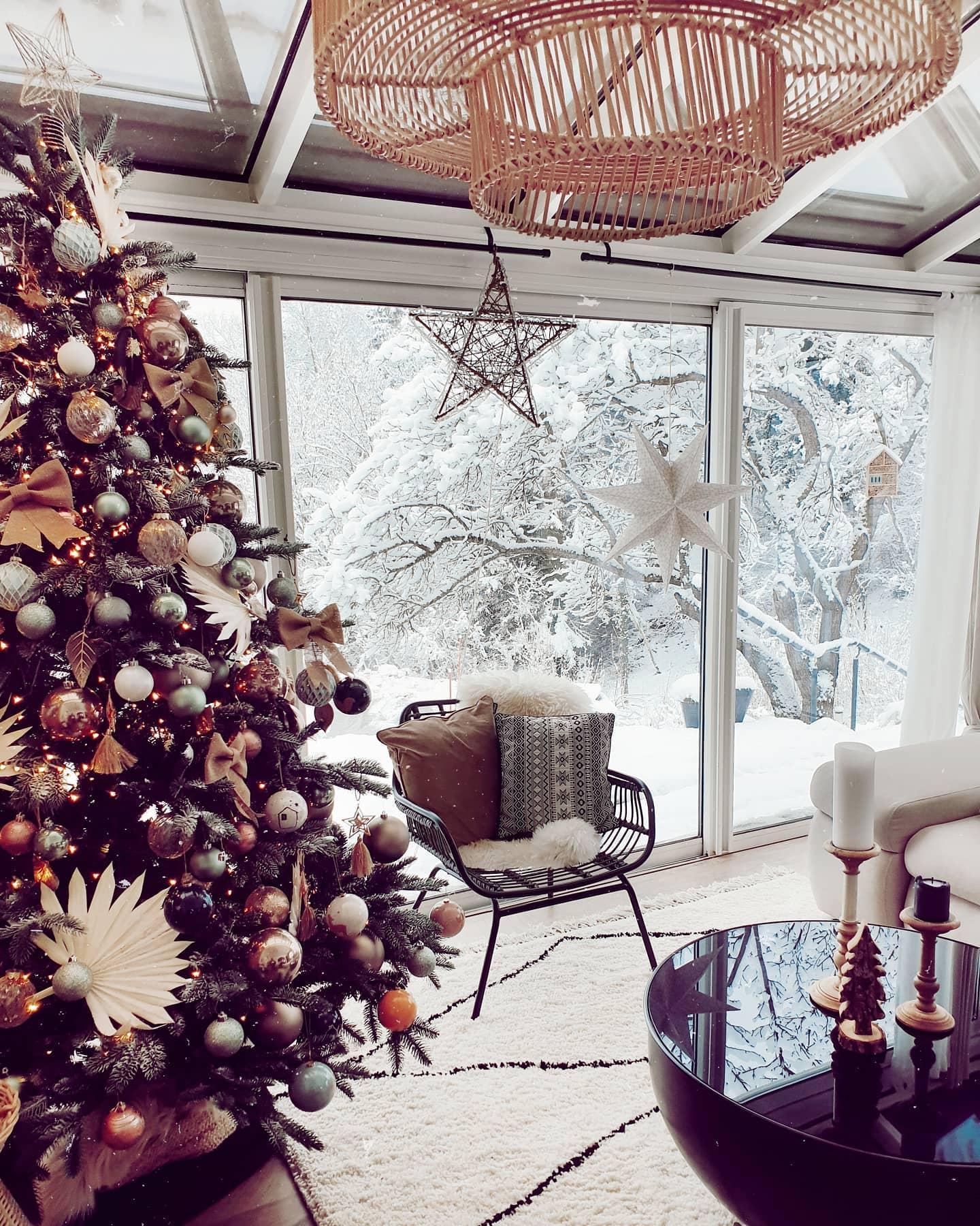 Zbliżenie na choinkę z ozdobami w kolorach ziemi na tle dużego okna oranżerii